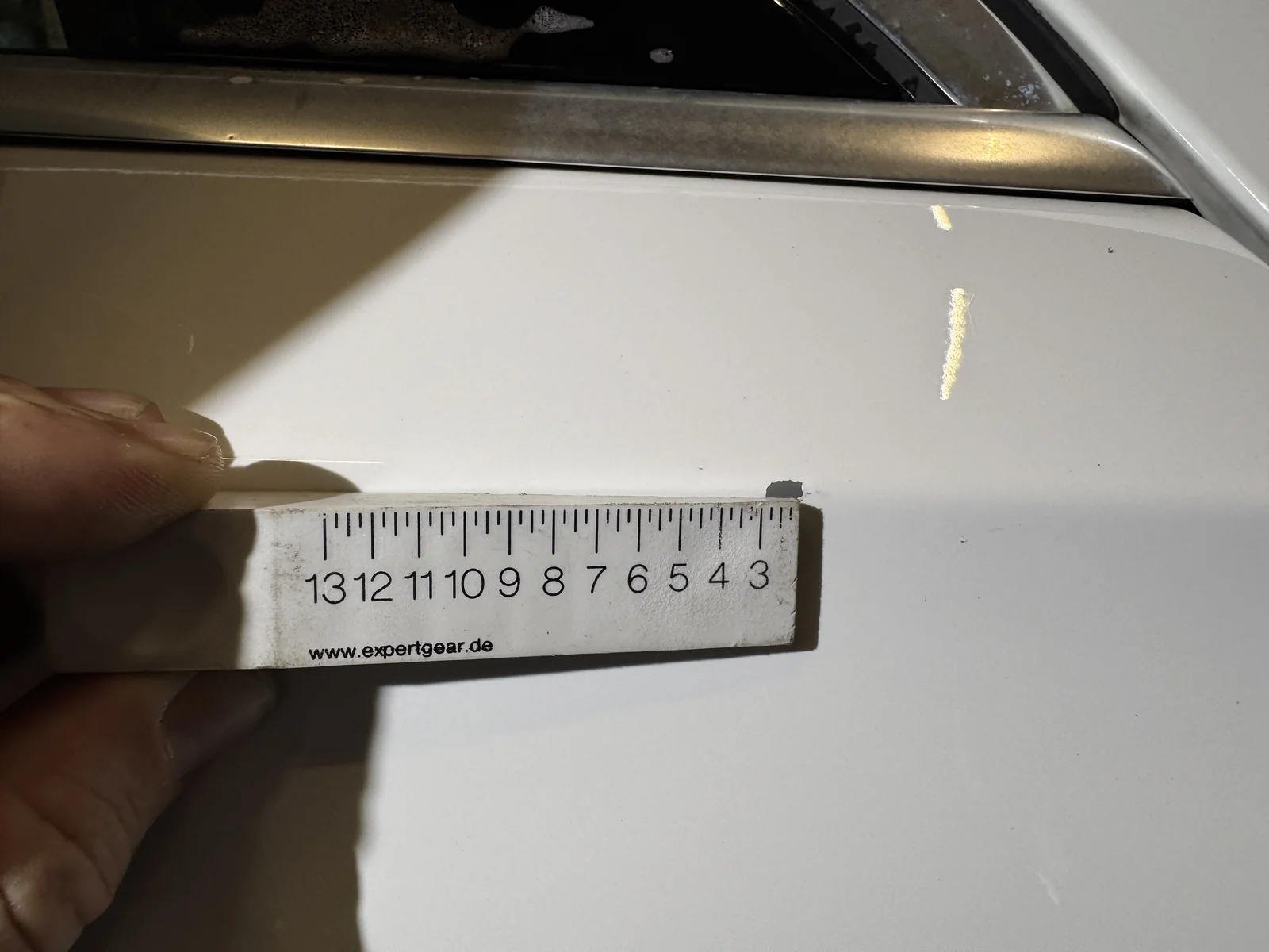 Detail der Lackbeschädigung an der weißen Fahrzeugtür mit angehaltenem Maßstab