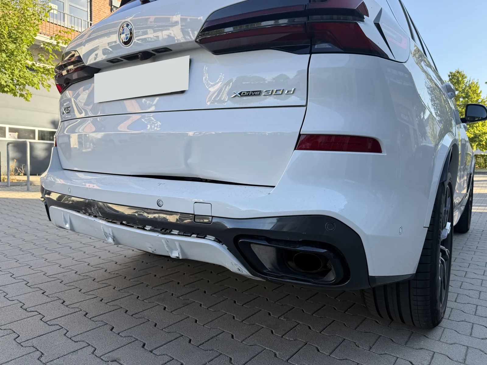 Weißer BMW X5 mit sichtbaren Beschädigungen an Heckklappe und Stoßfängerverkleidung; Kennzeichen anonymisiert